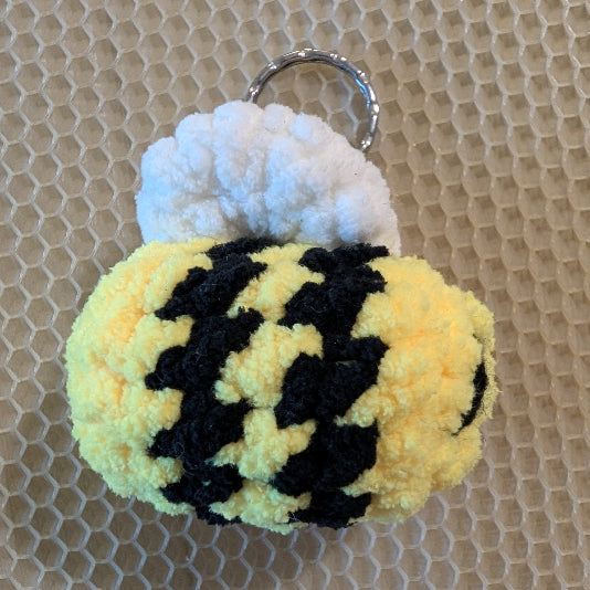 Crocheted bee keychain on a textured beige background